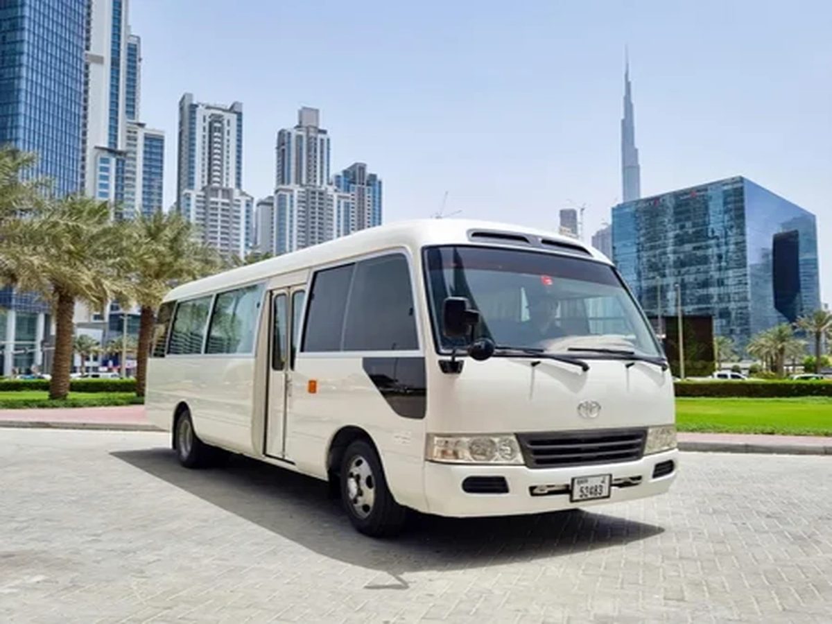 Toyota Coaster bus for daily car lift in Dubai with the city skyline behind